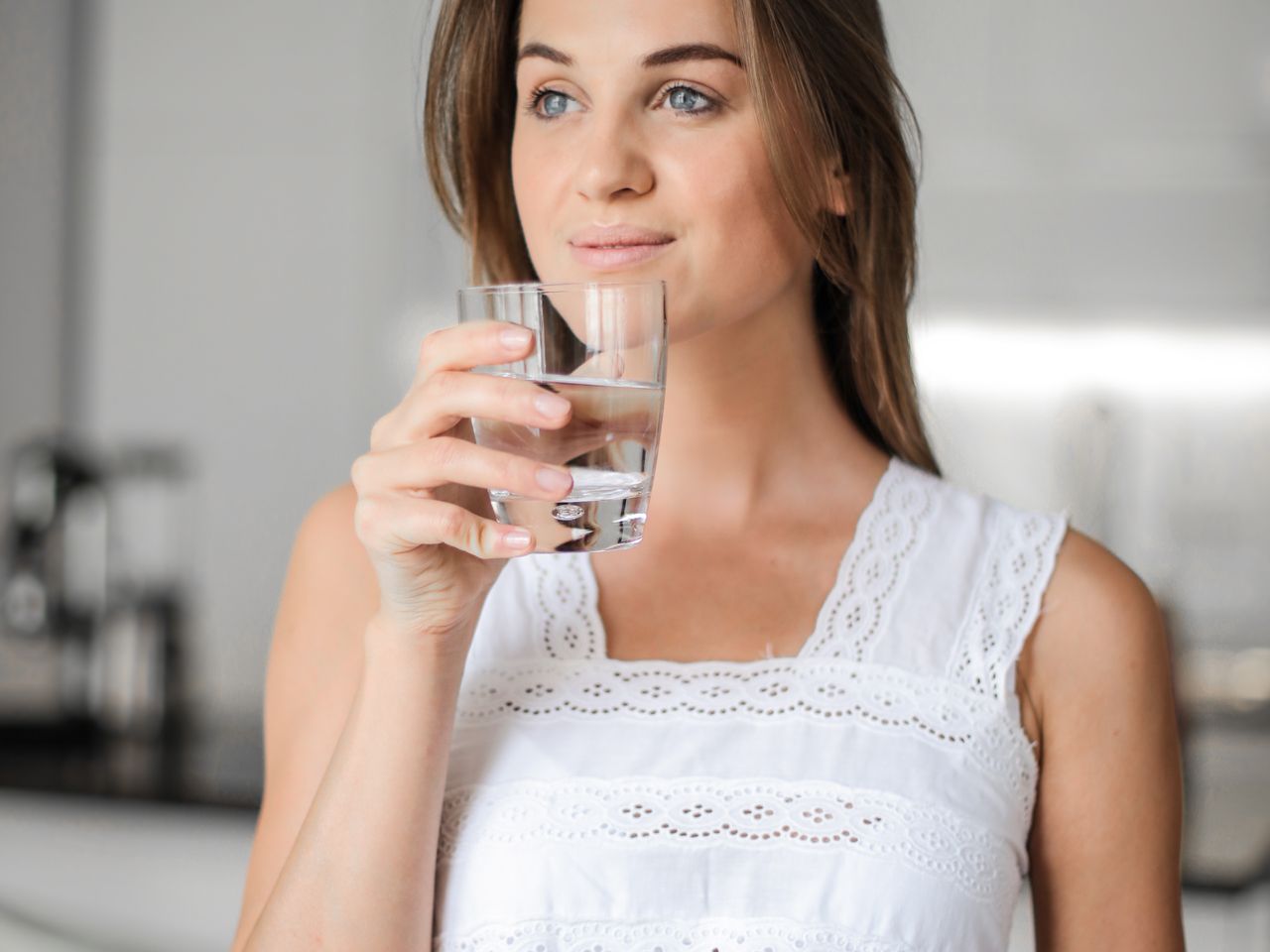 Mujer con ropa deportiva bebiendo un vaso de agua tras hacer ejercicio, asociado a h&aacute;bitos saludables y p&eacute;rdida de peso
