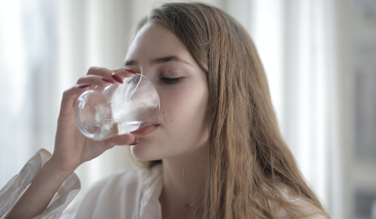 Persona bebiendo un vaso de agua para mantenerse hidratada y ayudar a controlar el az&uacute;car en sangre