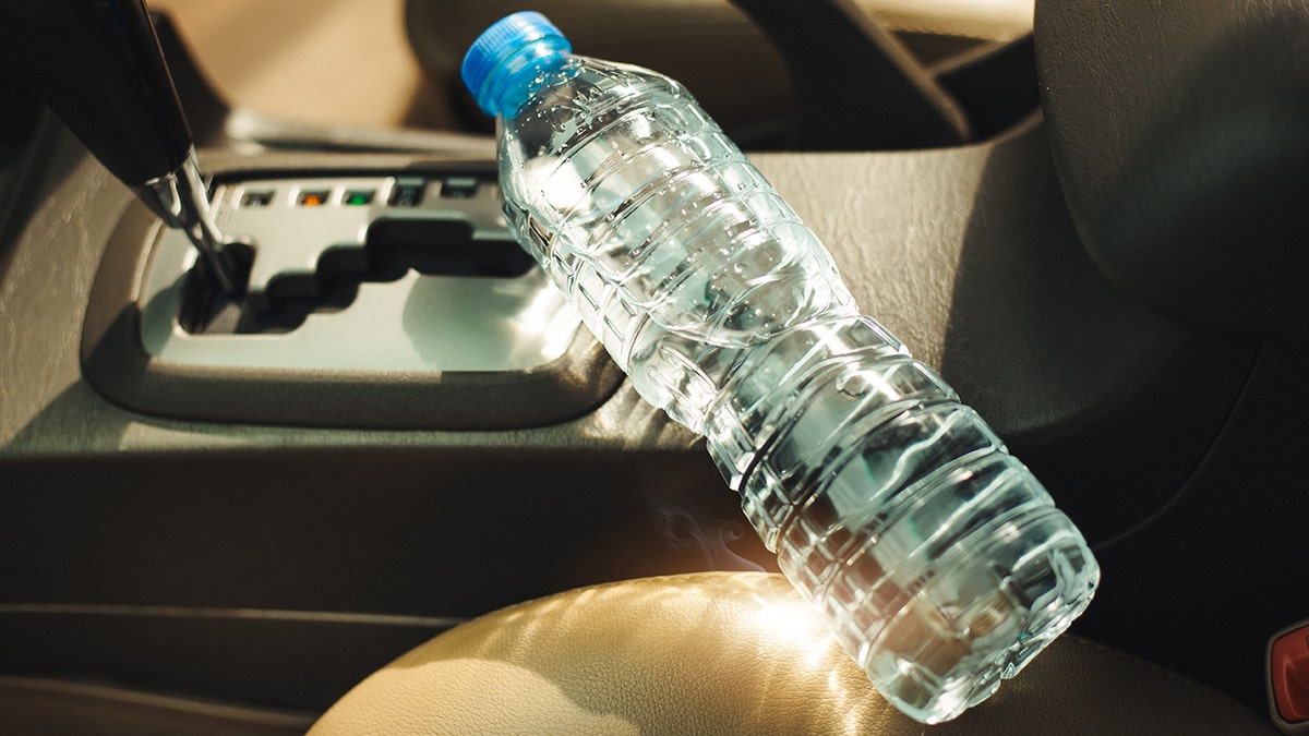 Botella de agua de pl&aacute;stico olvidada dentro de un coche bajo la luz intensa del sol de verano