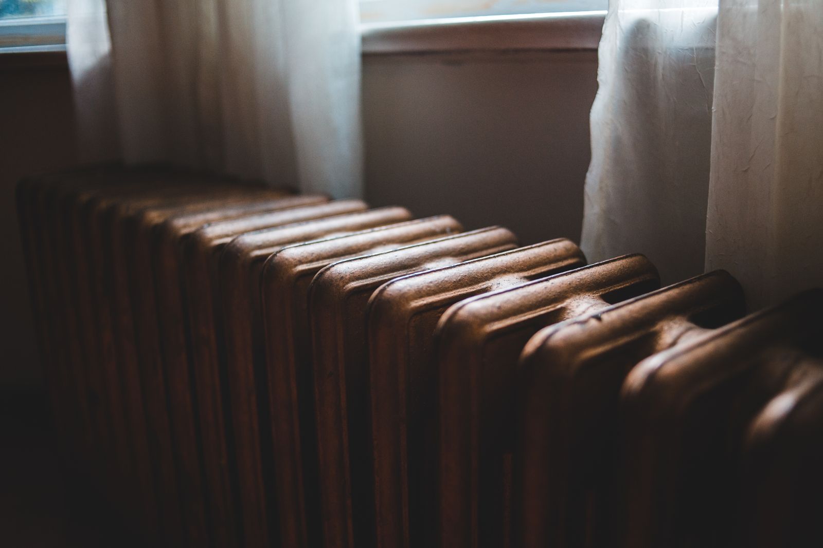 Radiador antiguo de hierro fundido junto a una ventana con cortinas blancas en una casa en invierno