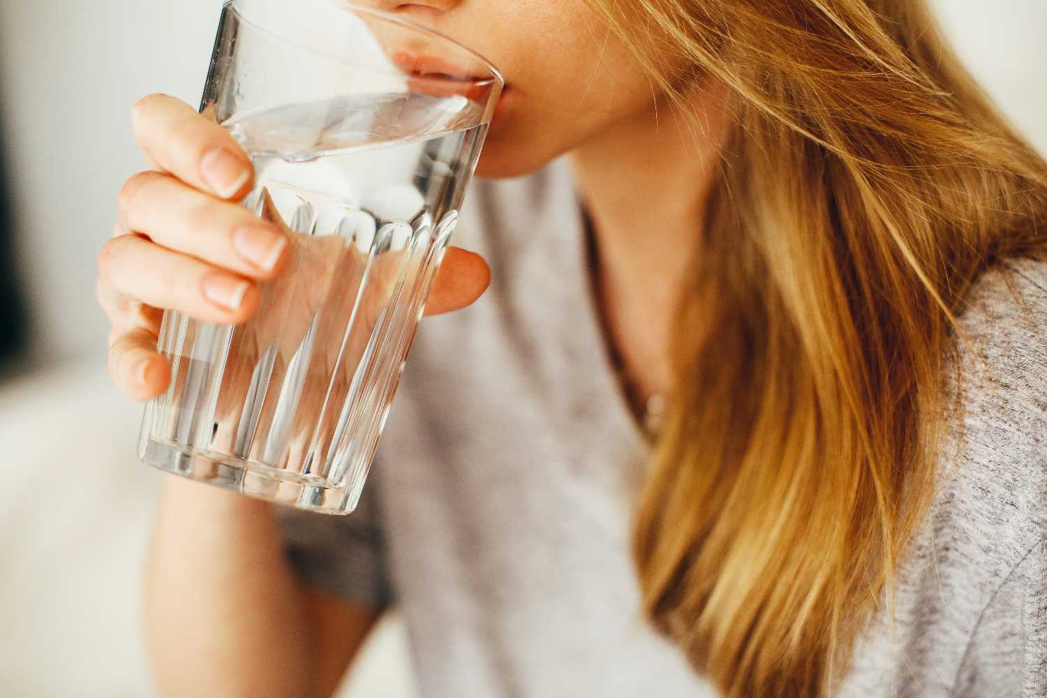 Persona sirvi&eacute;ndose un vaso de agua mineral para mantenerse hidratada a lo largo del d&iacute;a