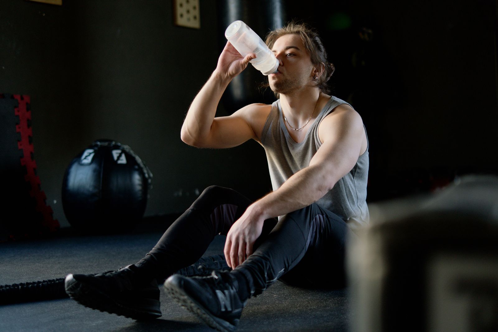 Hombre sentado en el suelo de un gimnasio bebiendo agua de una botella tras entrenar con pesas