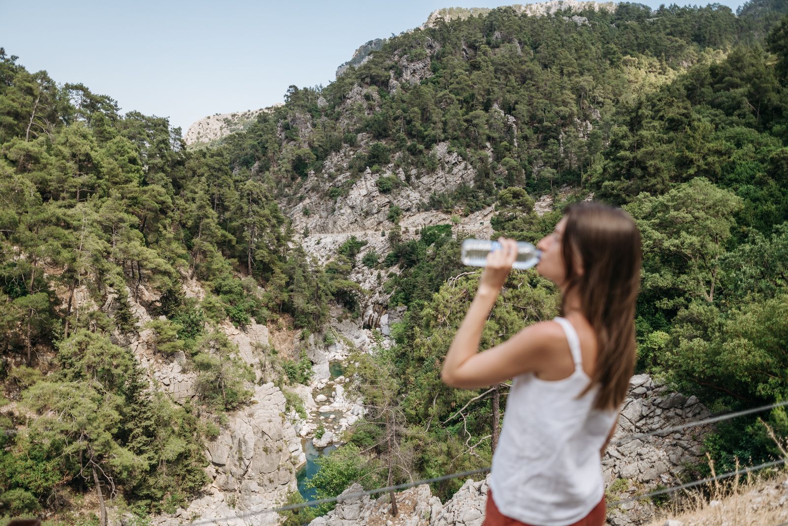 Senderista bebiendo agua de una botella en un mirador sobre un barranco con pinos y un r&iacute;o al fondo