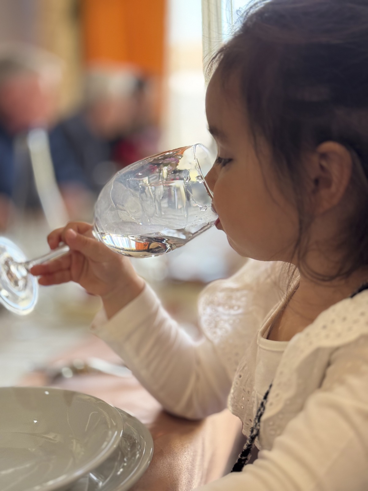 Ni&ntilde;a bebiendo un vaso de agua sentada a la mesa, ilustrando la hidrataci&oacute;n infantil diaria