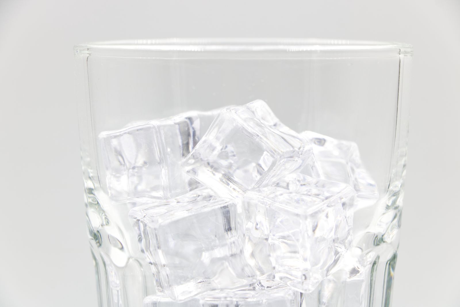 Cubitos de hielo transparentes dentro de un vaso de cristal sobre fondo claro