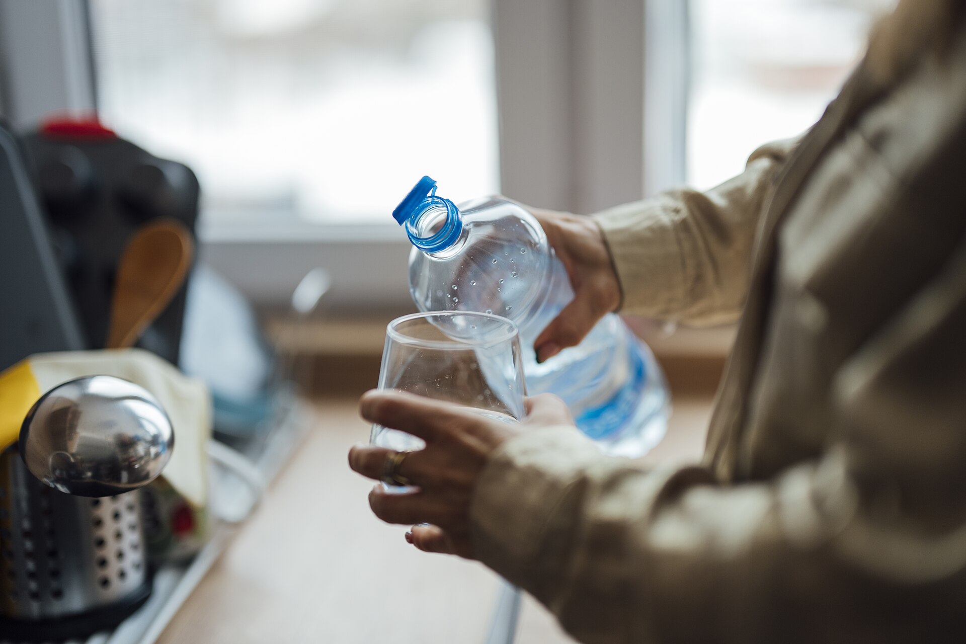 Persona sirviendo agua desde una botella a un vaso de cristal en una cocina con luz natural