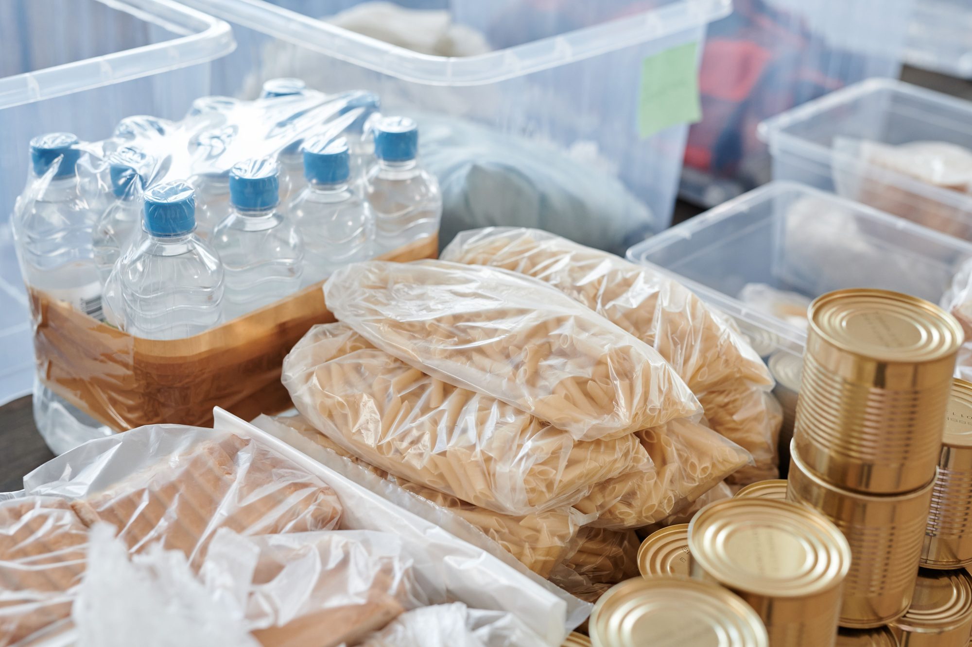 Despensa de emergencia en casa con un pack de botellas de agua, bolsas de pasta, latas de conserva y cajas de almacenaje transparentes