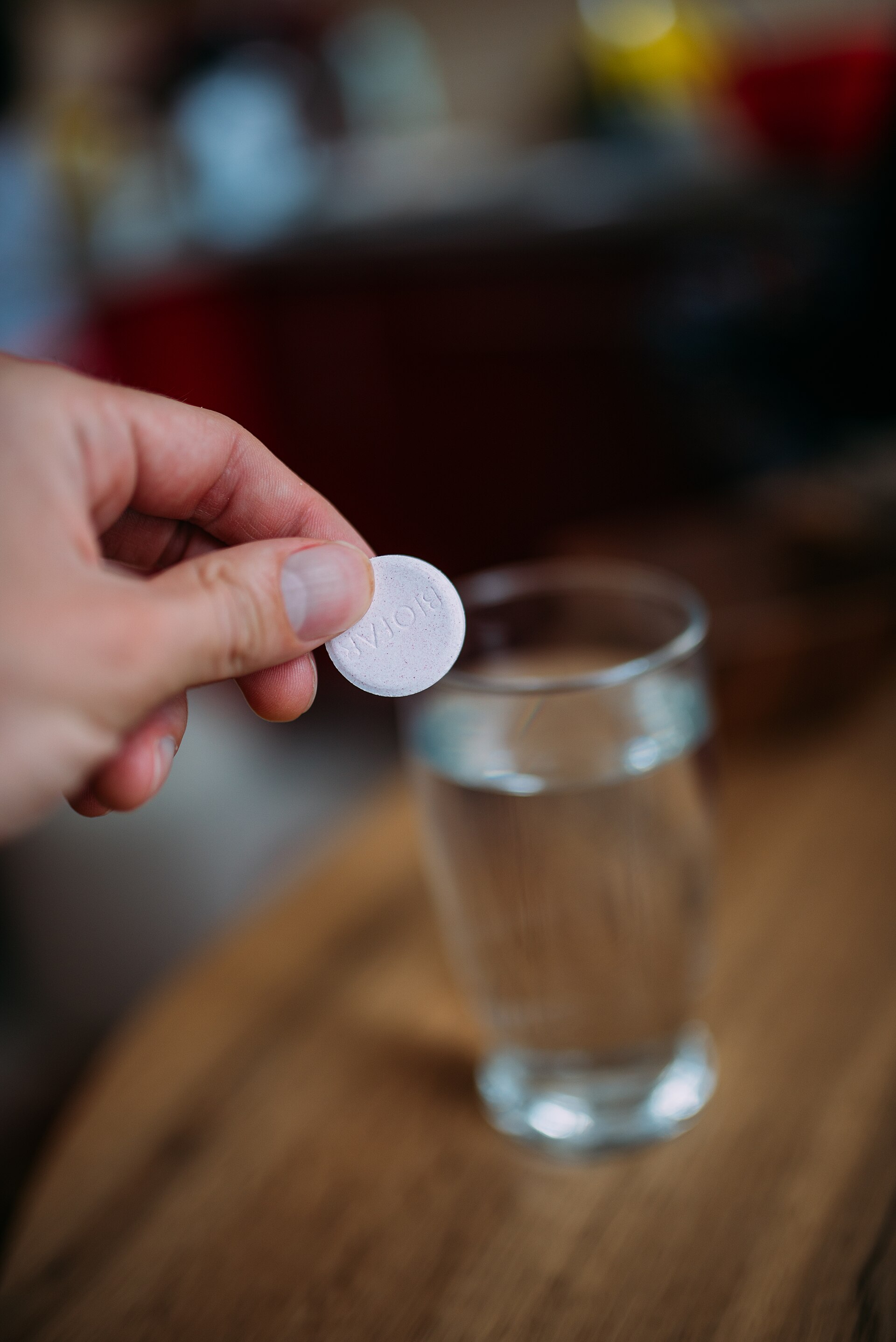 Mano sosteniendo un comprimido sobre un vaso de agua transparente